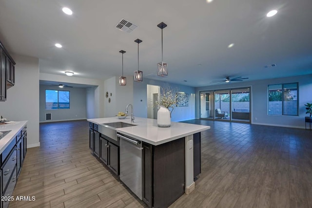 kitchen with sink, a kitchen island with sink, hanging light fixtures, stainless steel dishwasher, and light wood-type flooring