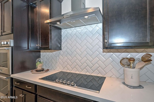 kitchen with backsplash, stainless steel double oven, dark brown cabinetry, wall chimney range hood, and black electric cooktop