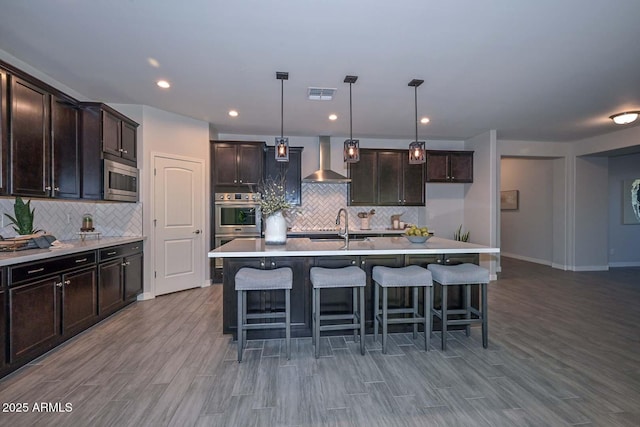 kitchen with decorative light fixtures, a center island with sink, and wall chimney exhaust hood