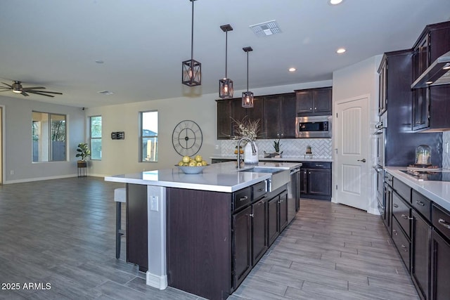 kitchen featuring decorative light fixtures, an island with sink, sink, light hardwood / wood-style floors, and stainless steel appliances