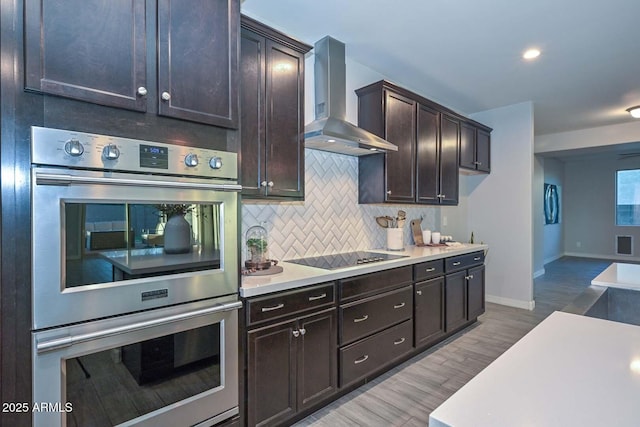 kitchen featuring hardwood / wood-style flooring, wall chimney exhaust hood, tasteful backsplash, black electric cooktop, and stainless steel double oven