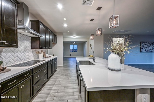 kitchen featuring sink, an island with sink, pendant lighting, wall chimney range hood, and backsplash