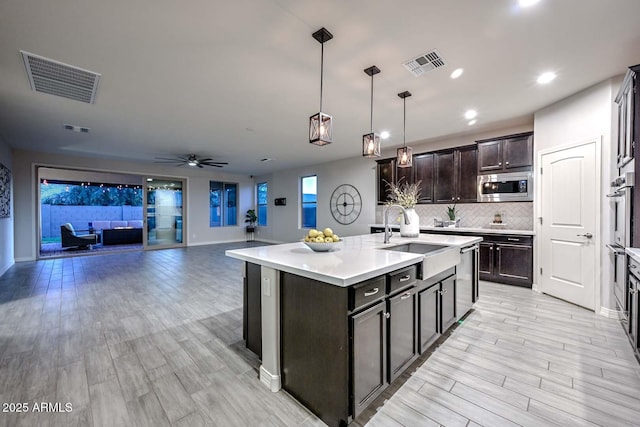 kitchen featuring sink, light wood-type flooring, an island with sink, pendant lighting, and stainless steel appliances