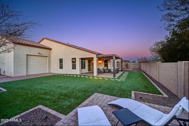 back house at dusk with a patio area and a lawn