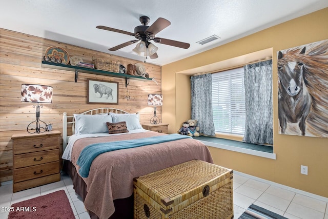 bedroom featuring wood walls, tile patterned flooring, visible vents, and a ceiling fan