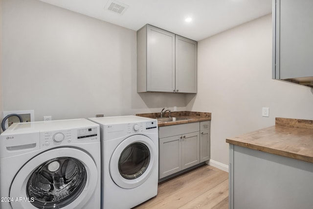 clothes washing area with cabinets, separate washer and dryer, sink, and light wood-type flooring