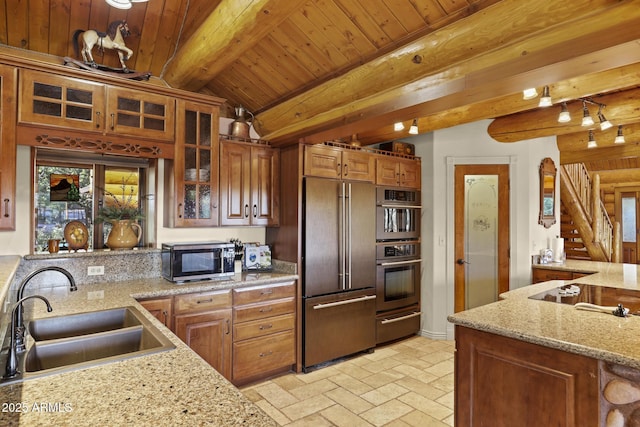 kitchen with sink, appliances with stainless steel finishes, vaulted ceiling with beams, light stone counters, and wooden ceiling