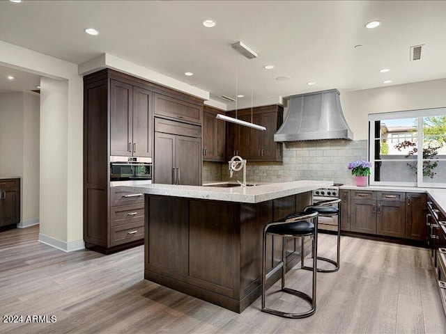 kitchen with backsplash, custom range hood, light hardwood / wood-style flooring, and appliances with stainless steel finishes