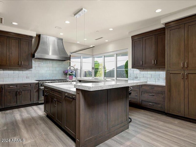 kitchen with backsplash, wall chimney range hood, and light wood-type flooring