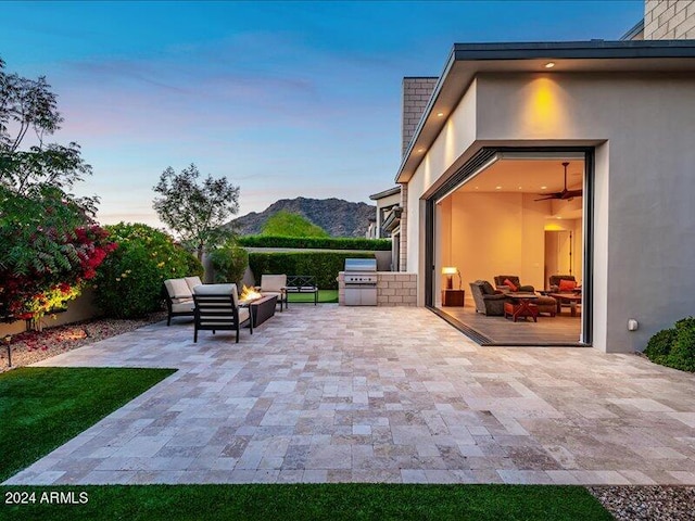 patio terrace at dusk with a mountain view, an outdoor living space, a grill, and exterior kitchen