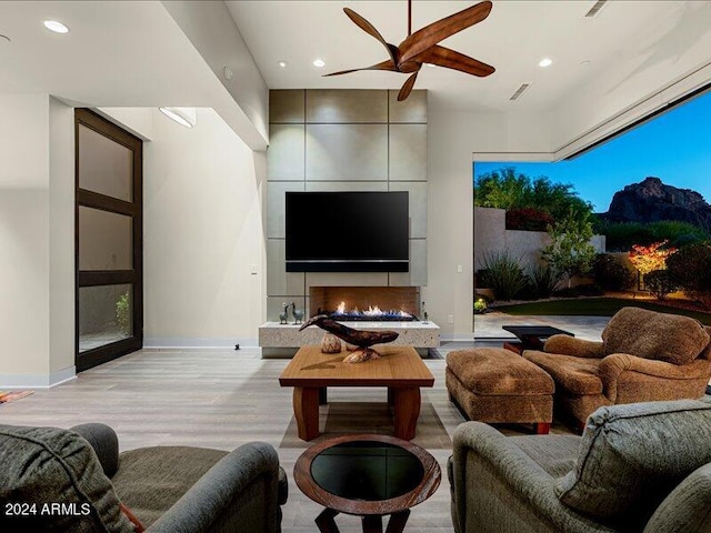 living room featuring a mountain view, a tile fireplace, ceiling fan, and light hardwood / wood-style floors