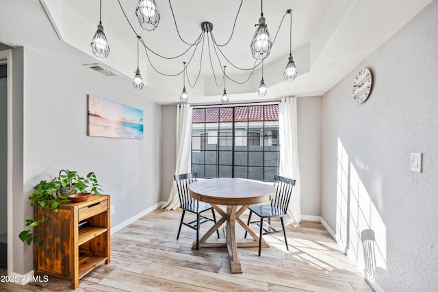 dining room featuring a tray ceiling, a chandelier, and light hardwood / wood-style floors