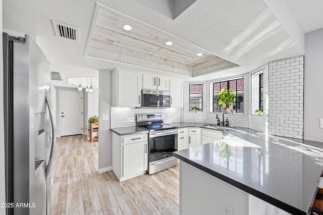 kitchen featuring sink, stainless steel appliances, kitchen peninsula, white cabinets, and a raised ceiling