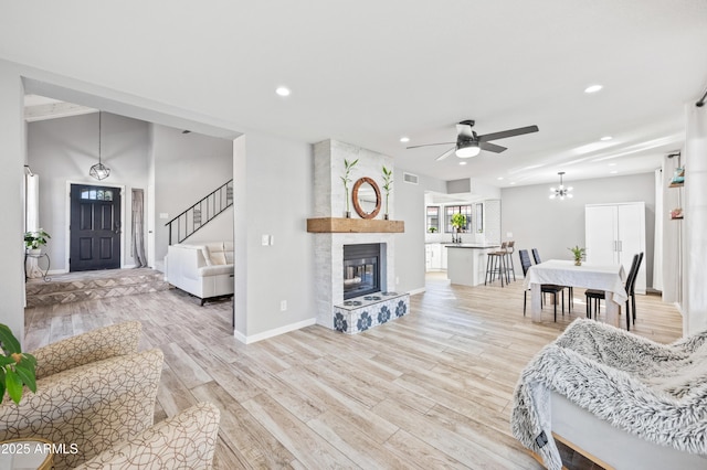 living room featuring a large fireplace, ceiling fan with notable chandelier, and light wood-type flooring