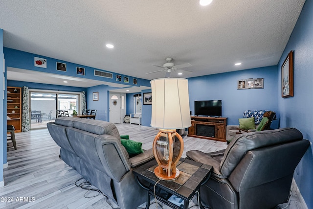 living room featuring ceiling fan, a fireplace, light wood-type flooring, and a textured ceiling