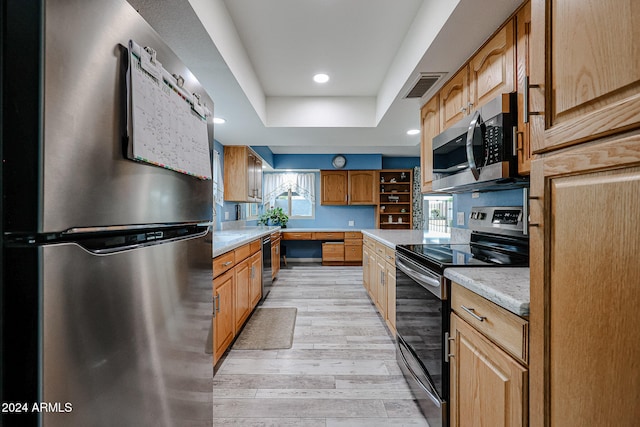 kitchen featuring black appliances, light stone countertops, a raised ceiling, and light wood-type flooring