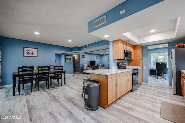 kitchen featuring kitchen peninsula, appliances with stainless steel finishes, a breakfast bar, a raised ceiling, and light hardwood / wood-style flooring