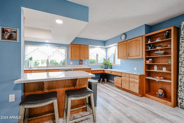 kitchen with sink, light wood-type flooring, a textured ceiling, a kitchen bar, and kitchen peninsula