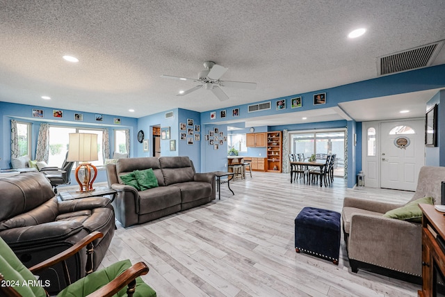 living room with a textured ceiling, light wood-type flooring, ceiling fan, and a healthy amount of sunlight