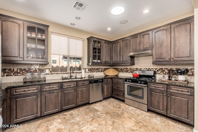 kitchen with backsplash, sink, dark stone countertops, appliances with stainless steel finishes, and dark brown cabinets