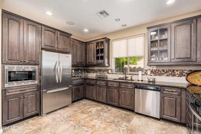 kitchen featuring sink, backsplash, dark stone countertops, dark brown cabinets, and appliances with stainless steel finishes