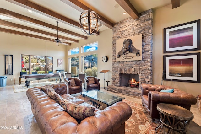 living room with ceiling fan with notable chandelier, beam ceiling, a stone fireplace, and a towering ceiling