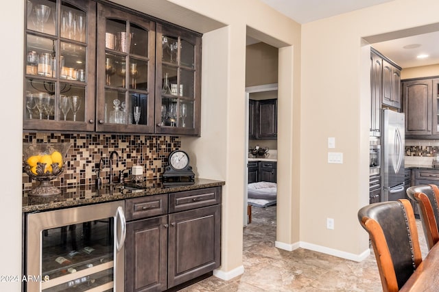 bar featuring dark brown cabinets, beverage cooler, and dark stone counters