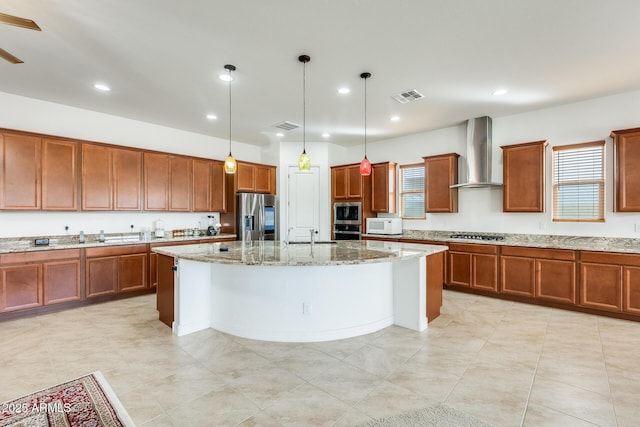 kitchen featuring visible vents, wall chimney exhaust hood, light stone counters, a center island, and stainless steel refrigerator with ice dispenser