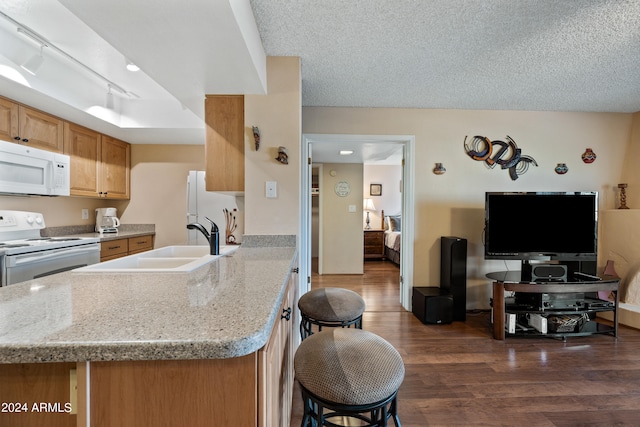 kitchen with dark hardwood / wood-style floors, sink, a breakfast bar area, rail lighting, and white appliances