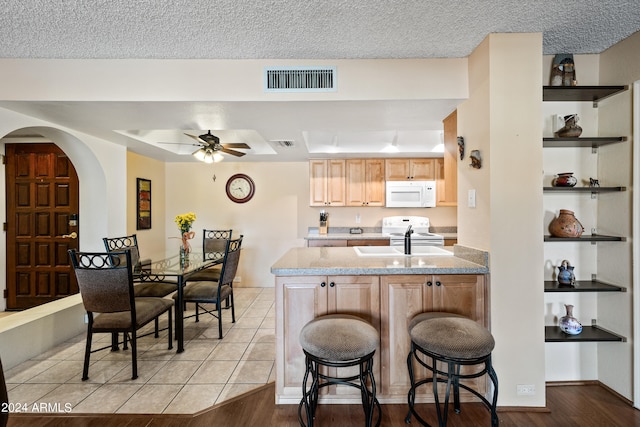 kitchen featuring light hardwood / wood-style floors, white appliances, a kitchen bar, light brown cabinetry, and ceiling fan