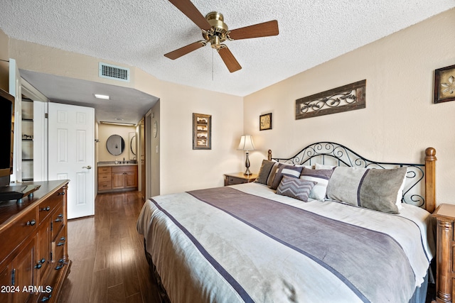 bedroom featuring ceiling fan, a textured ceiling, ensuite bathroom, and dark wood-type flooring