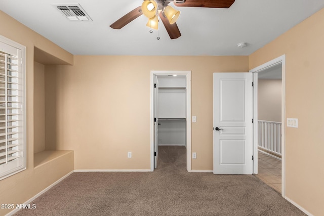 unfurnished bedroom with ceiling fan, light colored carpet, a closet, and a walk in closet