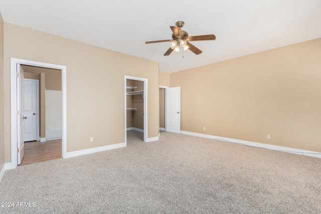 unfurnished bedroom with ceiling fan, a spacious closet, light carpet, and a closet