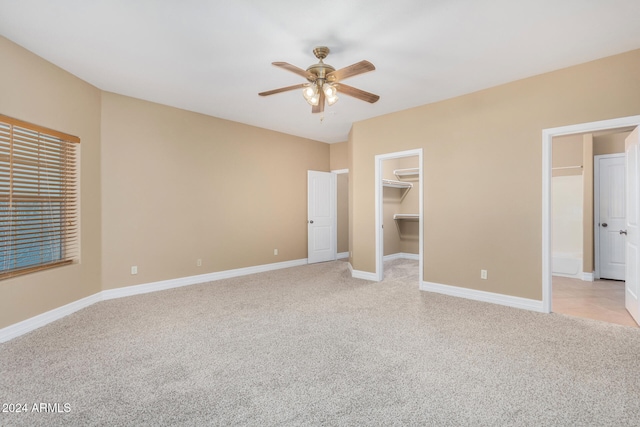 unfurnished bedroom featuring ceiling fan, light colored carpet, a walk in closet, and a closet