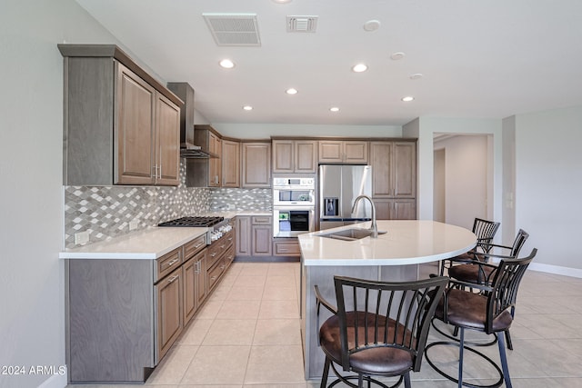 kitchen featuring stainless steel appliances, sink, an island with sink, wall chimney range hood, and light tile patterned flooring