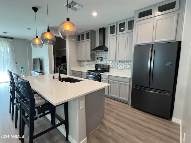 kitchen with wall chimney range hood, refrigerator, pendant lighting, sink, and black gas range oven