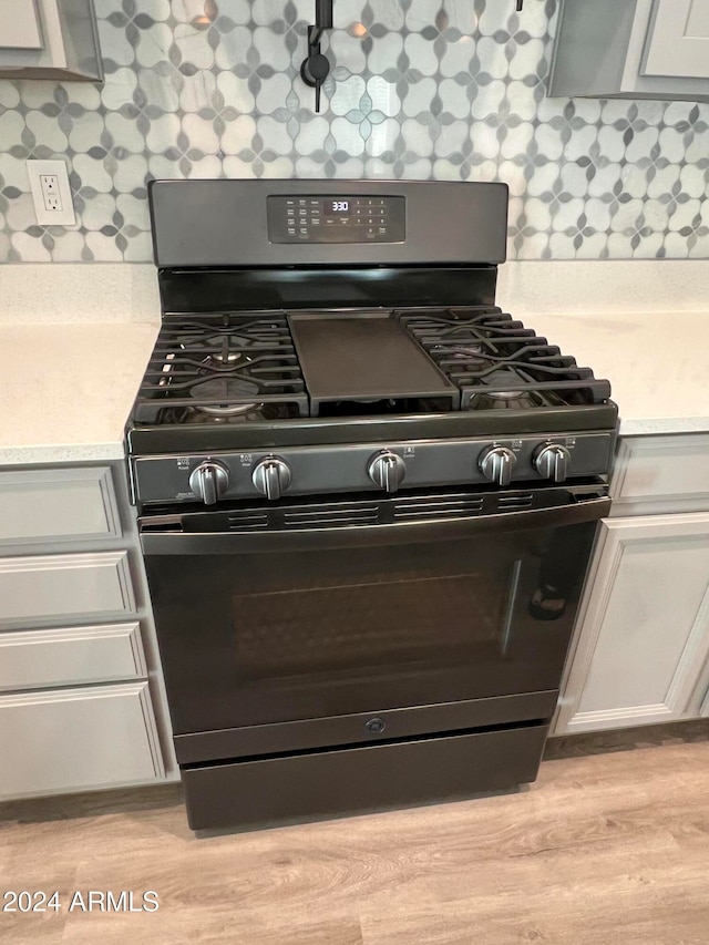 kitchen with black range with gas cooktop, light wood-type flooring, and tasteful backsplash