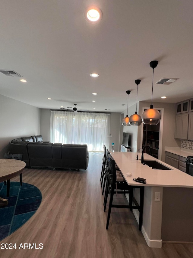 kitchen featuring sink, an island with sink, hanging light fixtures, ceiling fan, and hardwood / wood-style flooring