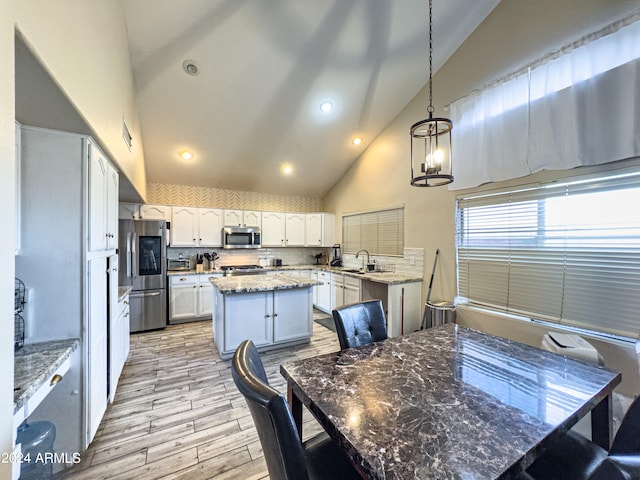 kitchen with dark stone counters, stainless steel appliances, white cabinets, a center island, and hanging light fixtures