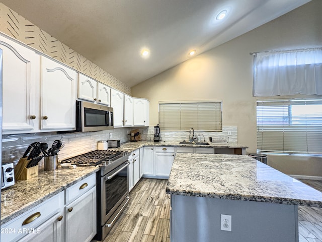 kitchen featuring light stone counters, white cabinets, stainless steel appliances, and vaulted ceiling