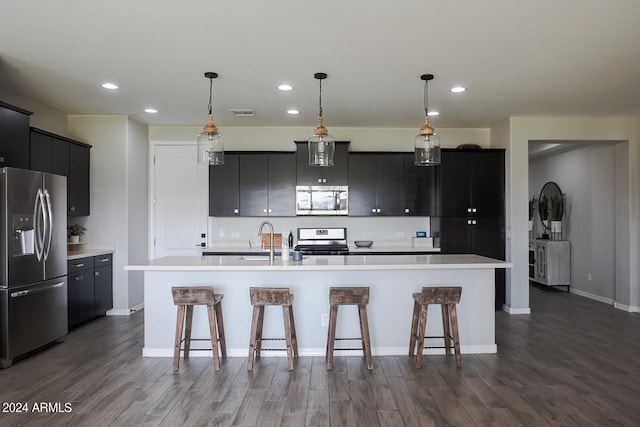 kitchen with dark hardwood / wood-style floors, a kitchen breakfast bar, an island with sink, and appliances with stainless steel finishes