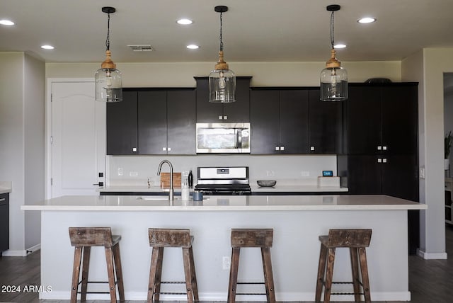 kitchen featuring decorative light fixtures, a kitchen breakfast bar, stainless steel appliances, and a kitchen island with sink