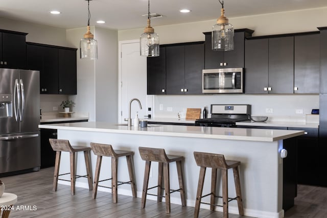 kitchen featuring wood-type flooring, stainless steel appliances, hanging light fixtures, and an island with sink