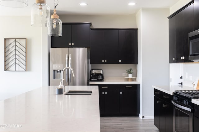 kitchen with sink, light wood-type flooring, hanging light fixtures, and appliances with stainless steel finishes