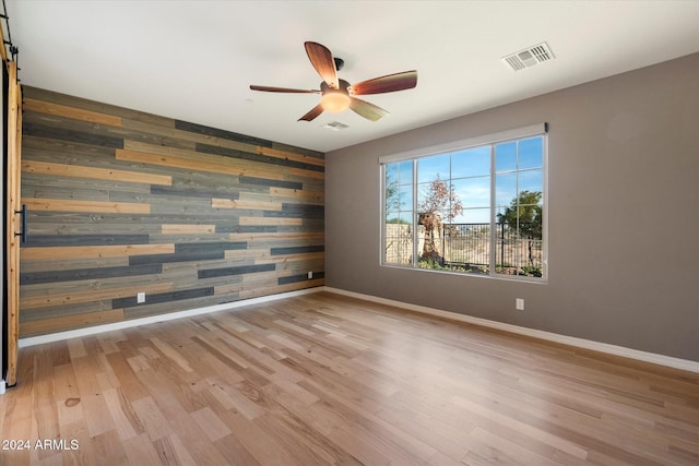 spare room featuring ceiling fan, a barn door, wooden walls, and light hardwood / wood-style flooring