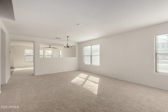 unfurnished room featuring a healthy amount of sunlight, light carpet, baseboards, and ceiling fan with notable chandelier
