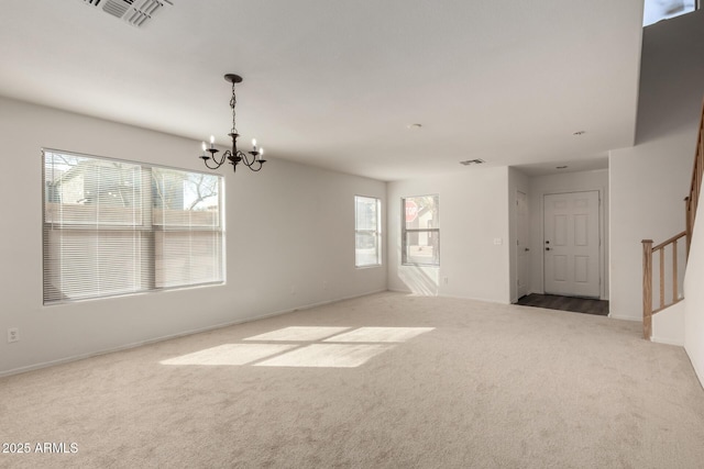 carpeted spare room featuring a healthy amount of sunlight, visible vents, an inviting chandelier, and stairs