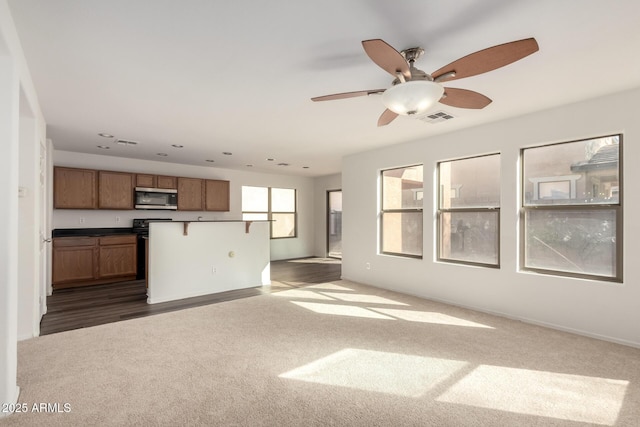 kitchen featuring dark carpet, brown cabinets, stainless steel microwave, and open floor plan