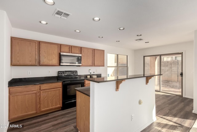 kitchen featuring visible vents, dark countertops, stainless steel microwave, a kitchen breakfast bar, and black electric range