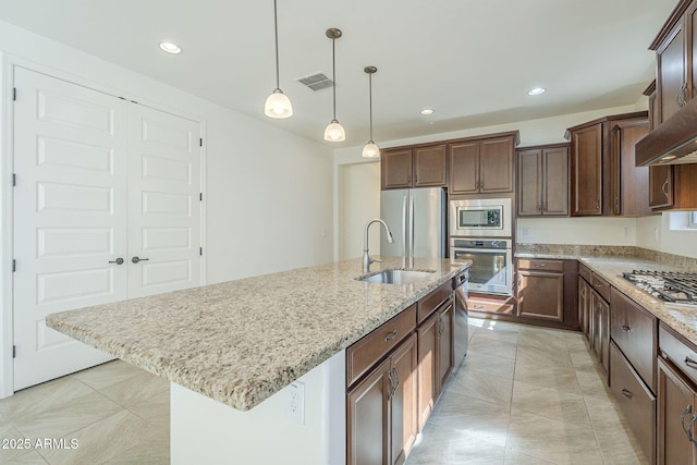 kitchen featuring stainless steel appliances, a sink, light stone counters, a kitchen island with sink, and recessed lighting